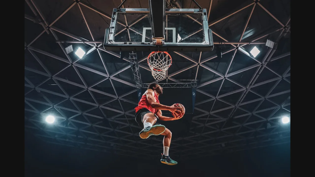 Photograph of a basketball player leaping toward the hoop for a dunk in a dark arena